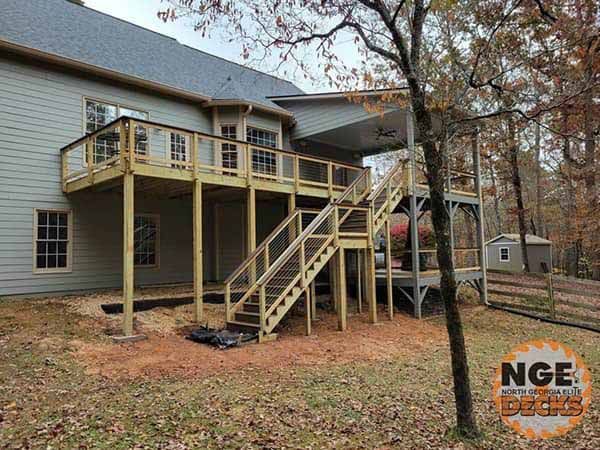 Wooden deck with stairs attached to a two-story beige house; exterior, natural setting.