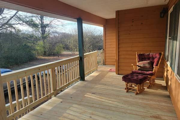 Wooden porch with rocking chair; overlooking trees and a car.