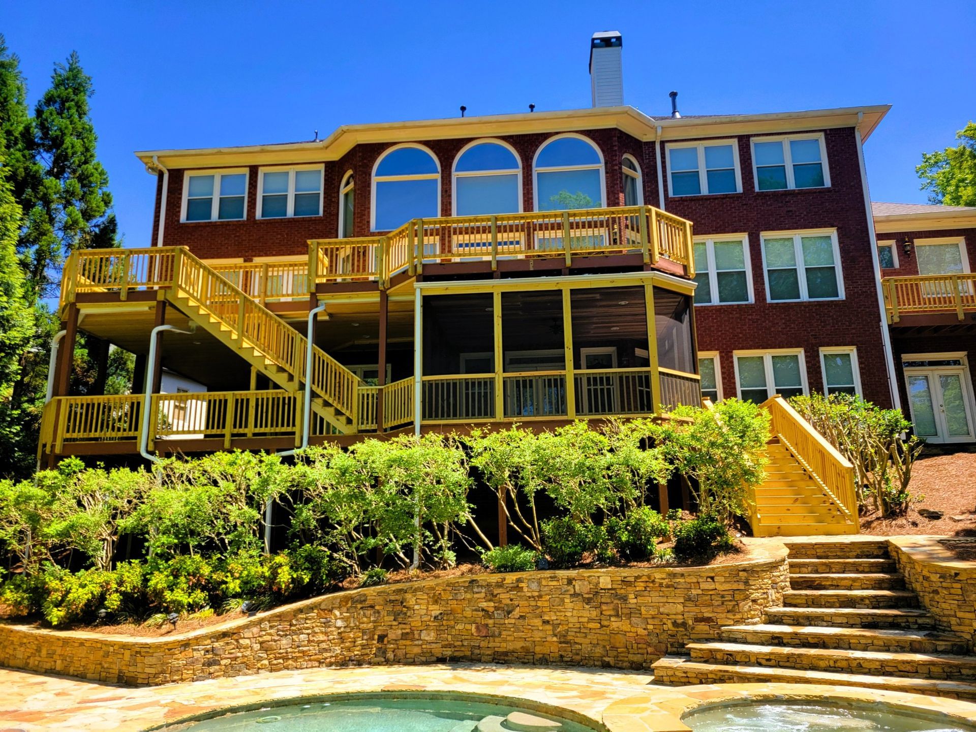 Brick house with multiple wooden decks and stairs, overlooking a pool.
