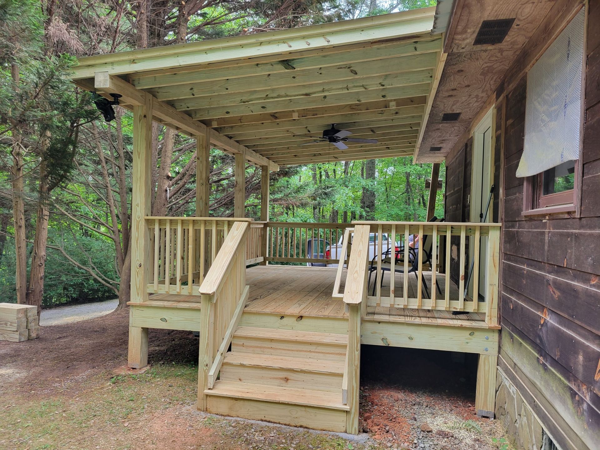 Wooden porch with steps, railing, and lattice ceiling, attached to a brown house; outdoors.