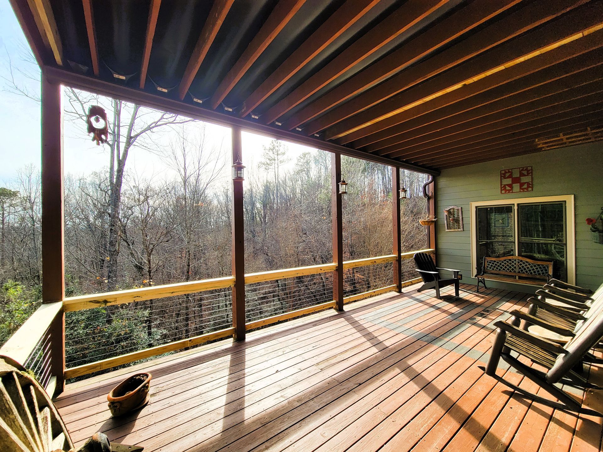 Wooden porch overlooking a forest. Several rocking chairs and a bench are visible.