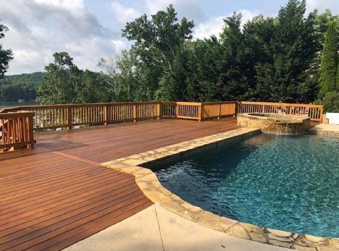 Wooden deck with a swimming pool and trees in the background.