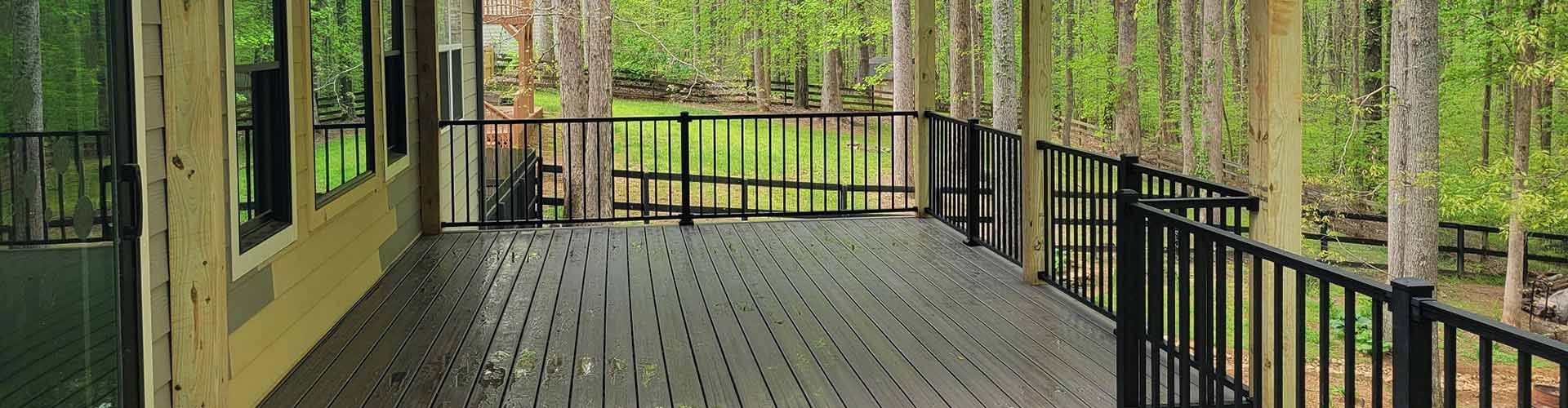 Wooden deck with black railings overlooking a green, wooded area.