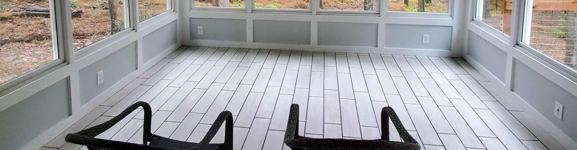 Sunroom with white painted wood floors and light gray walls, two black chairs are in the foreground.