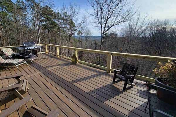 Wooden deck with railing, grill, chairs, and view of trees and distant hills.