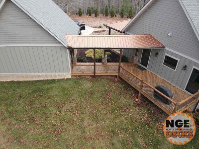 Wooden deck with copper roof connecting two houses; green grass in foreground.