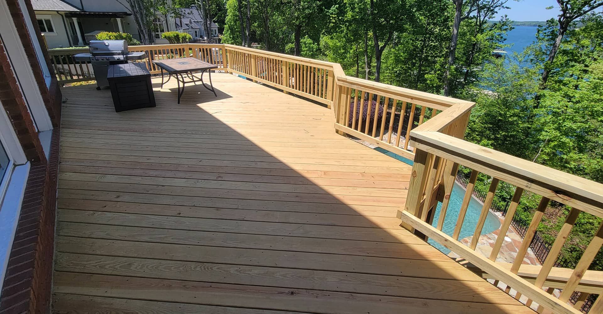 Wooden deck with railing, table, grill, and view of water.