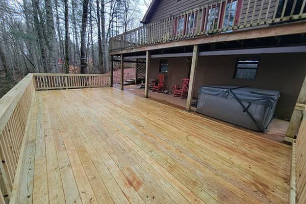 Wooden deck with a hot tub and a house in a forest.