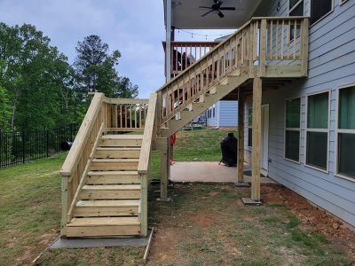 Wooden staircase leading to a second-story deck, attached to a light blue house, situated outdoors.