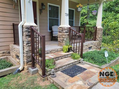Stone facade home entrance with brown metal railings, steps, and porch with hanging flowers.