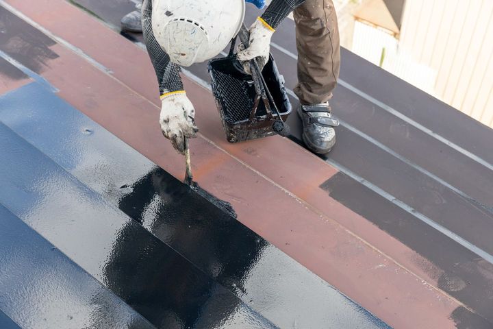 a man is painting a roof with black paint