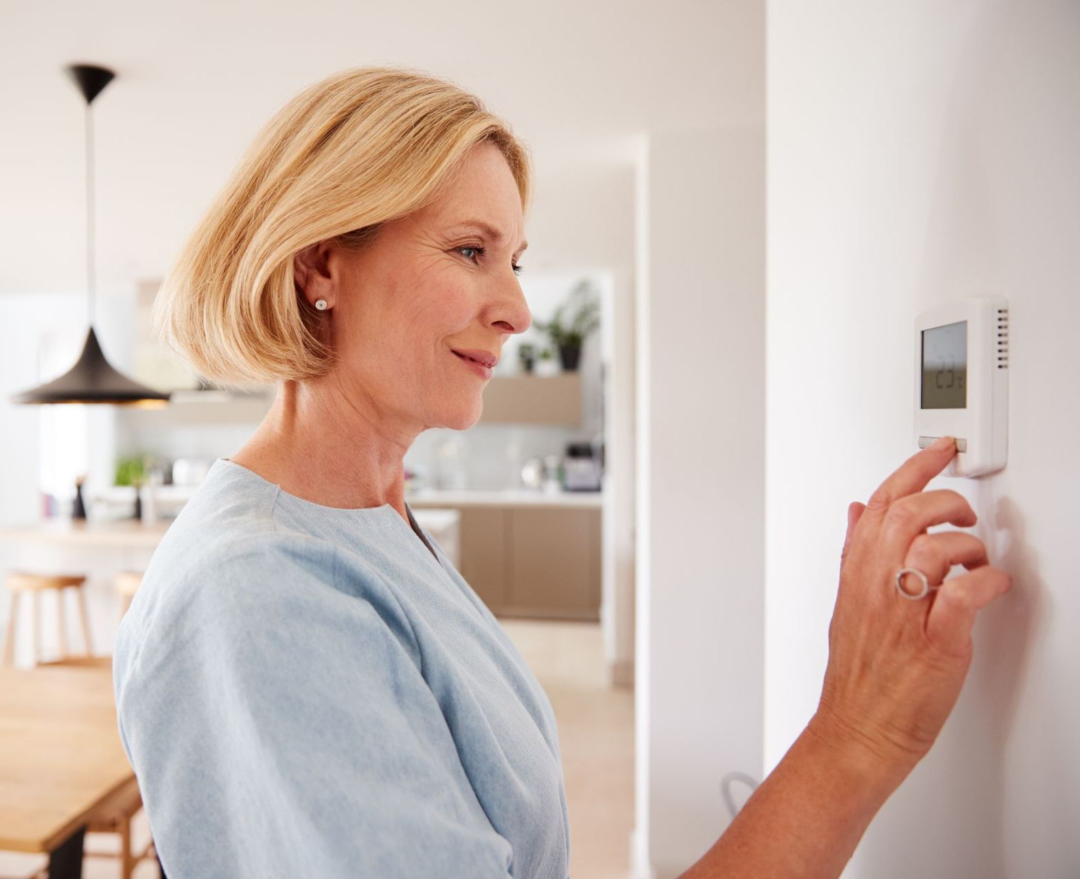 A woman is adjusting her thermostat in a living room.
