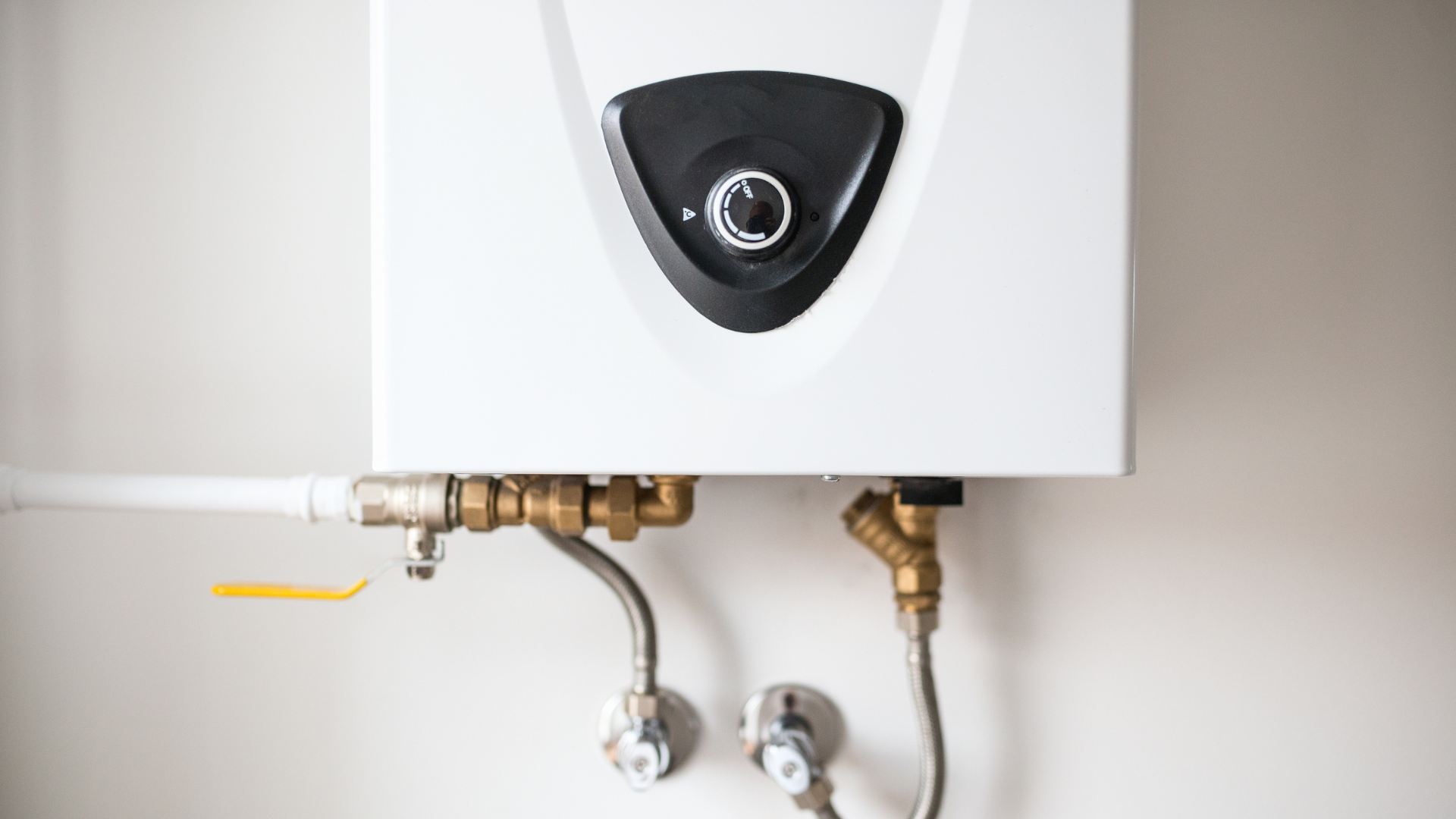 A white water heater is hanging on a white wall.