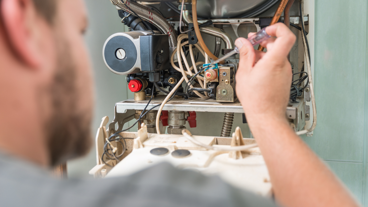 A man is fixing a boiler with a screwdriver.