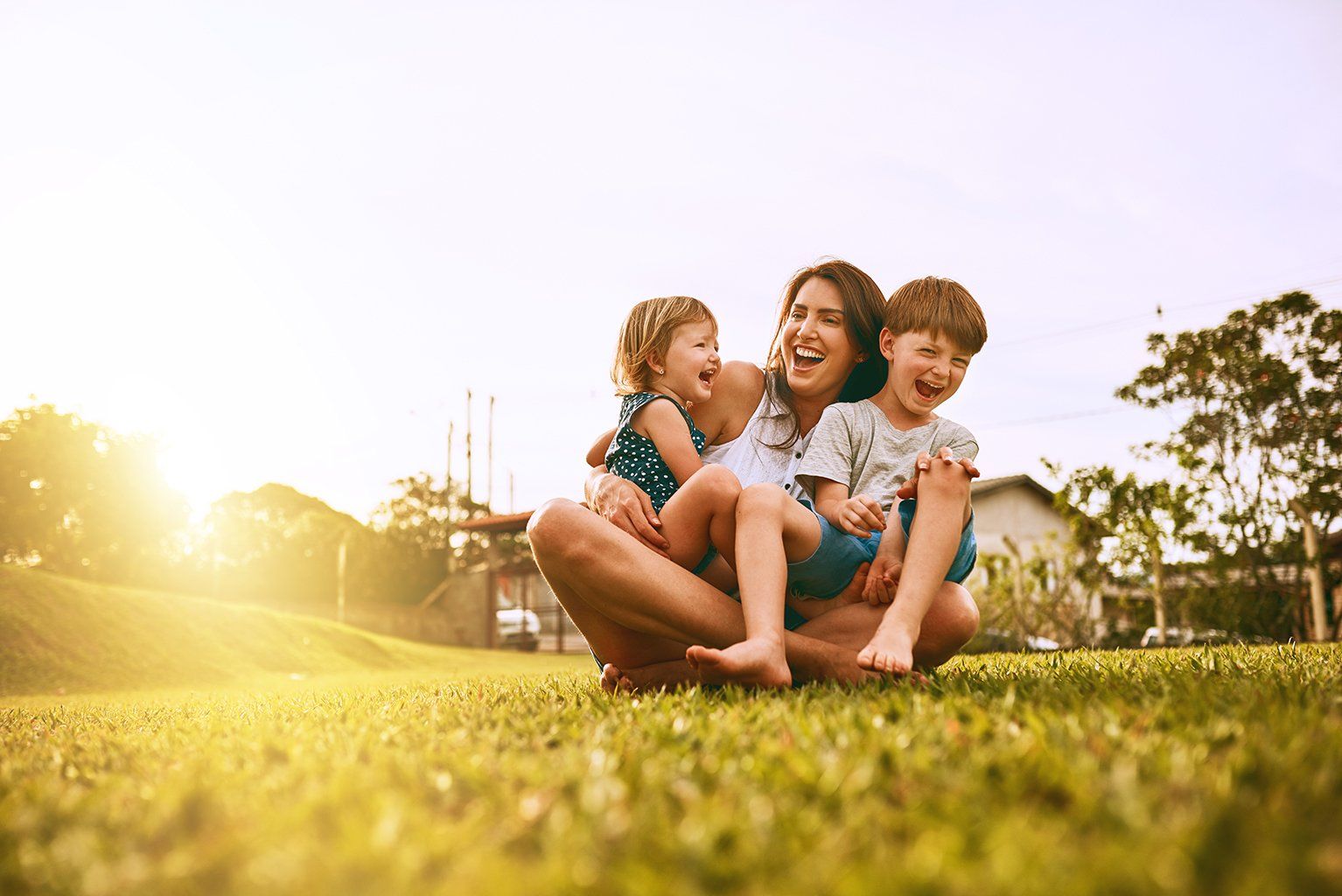 A woman is sitting on the grass with two children.