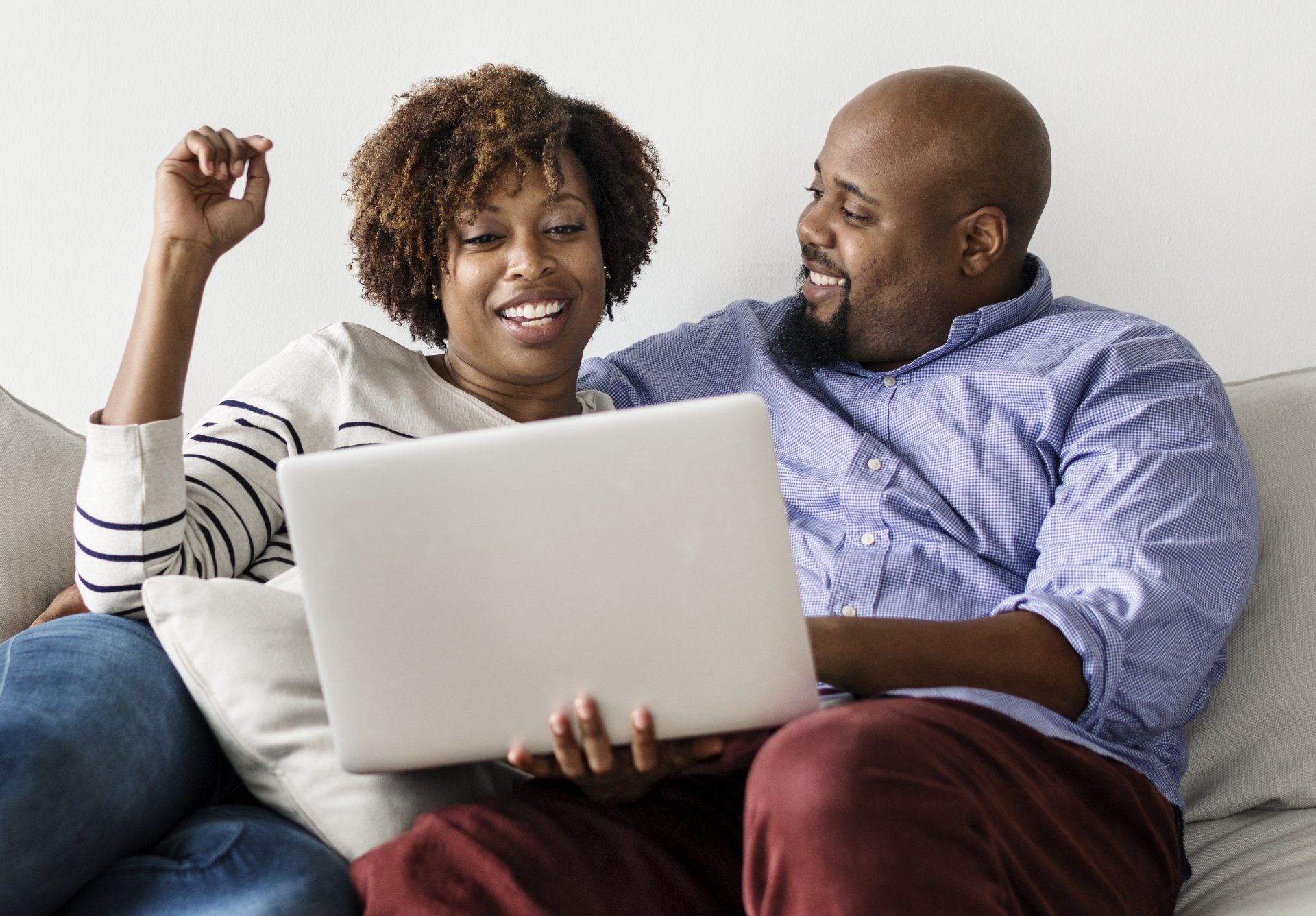 A man and a woman are sitting on a couch looking at a laptop.