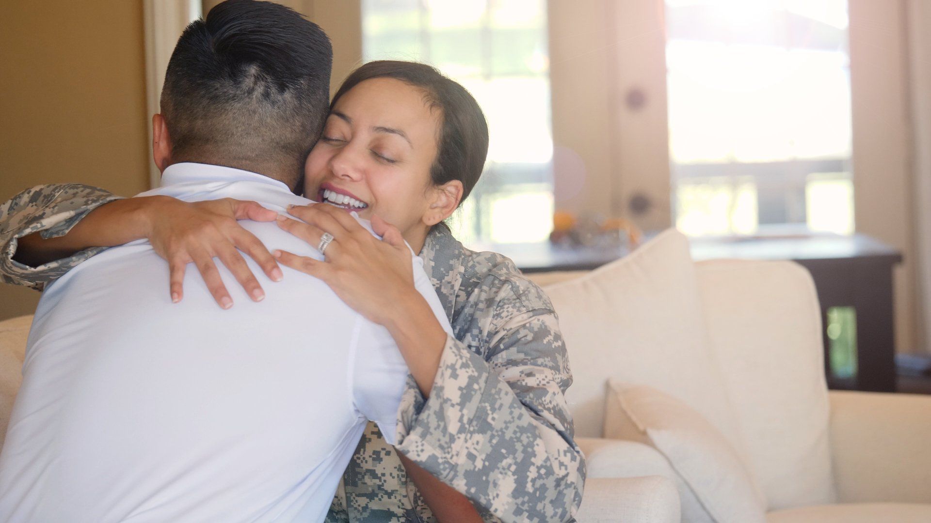 A woman in a military uniform is hugging a man on a couch.