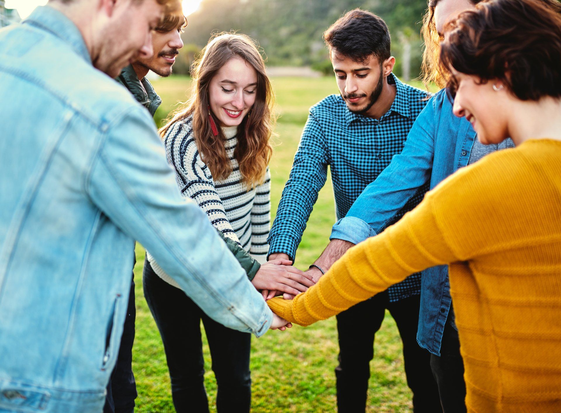 A group of young people are putting their hands together in a circle.
