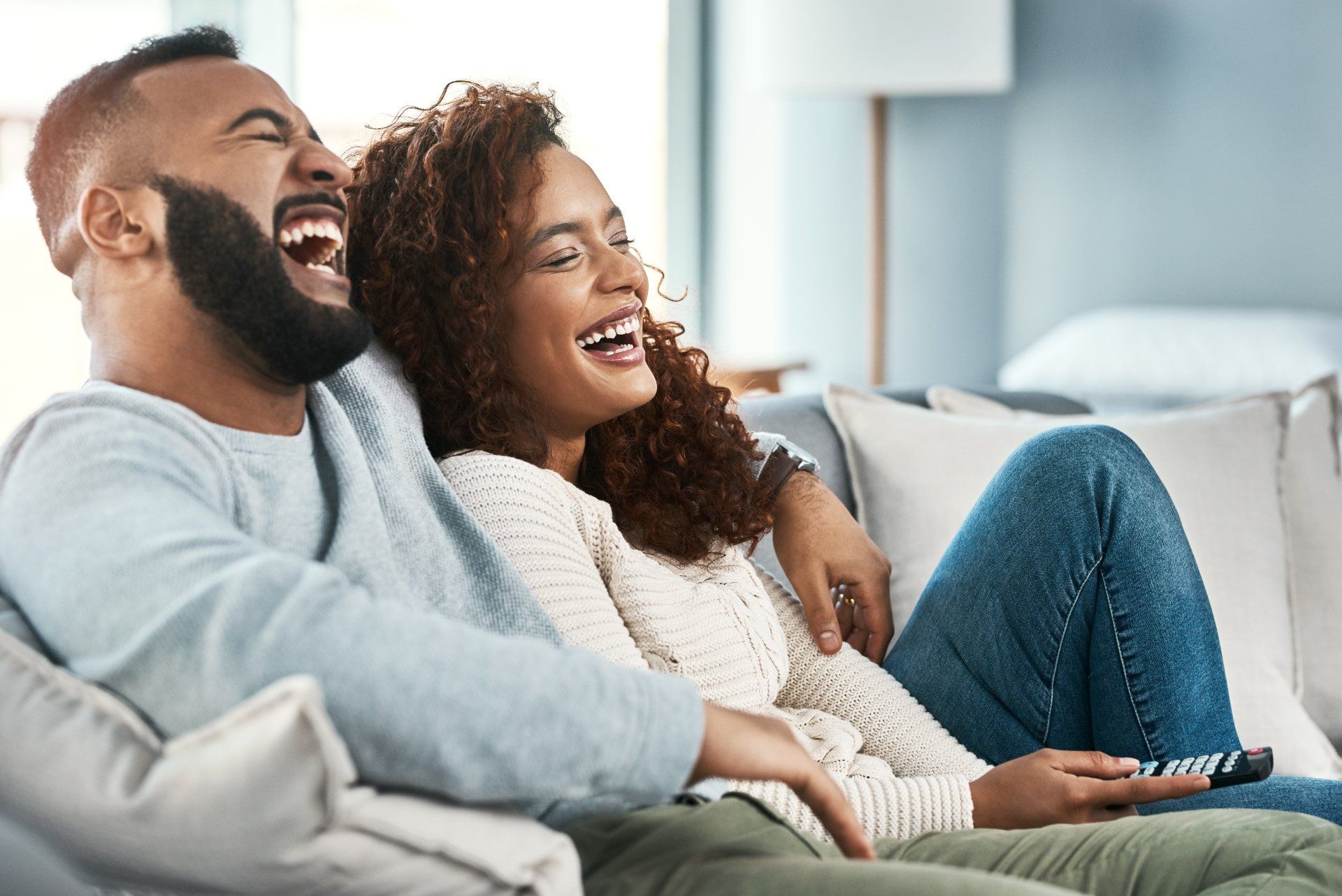 A man and a woman are laughing while sitting on a couch.