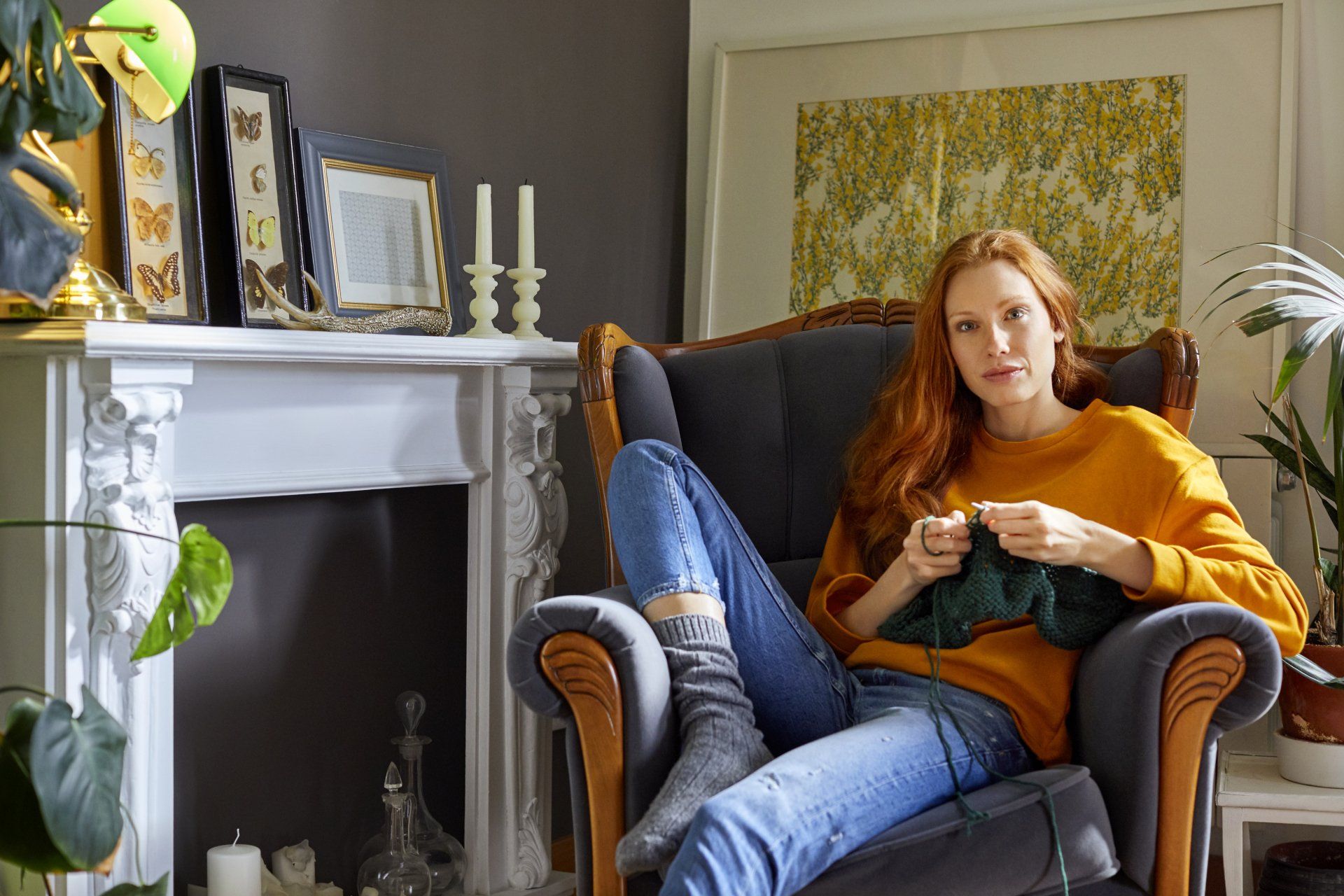 A woman is sitting in a chair knitting in a living room.
