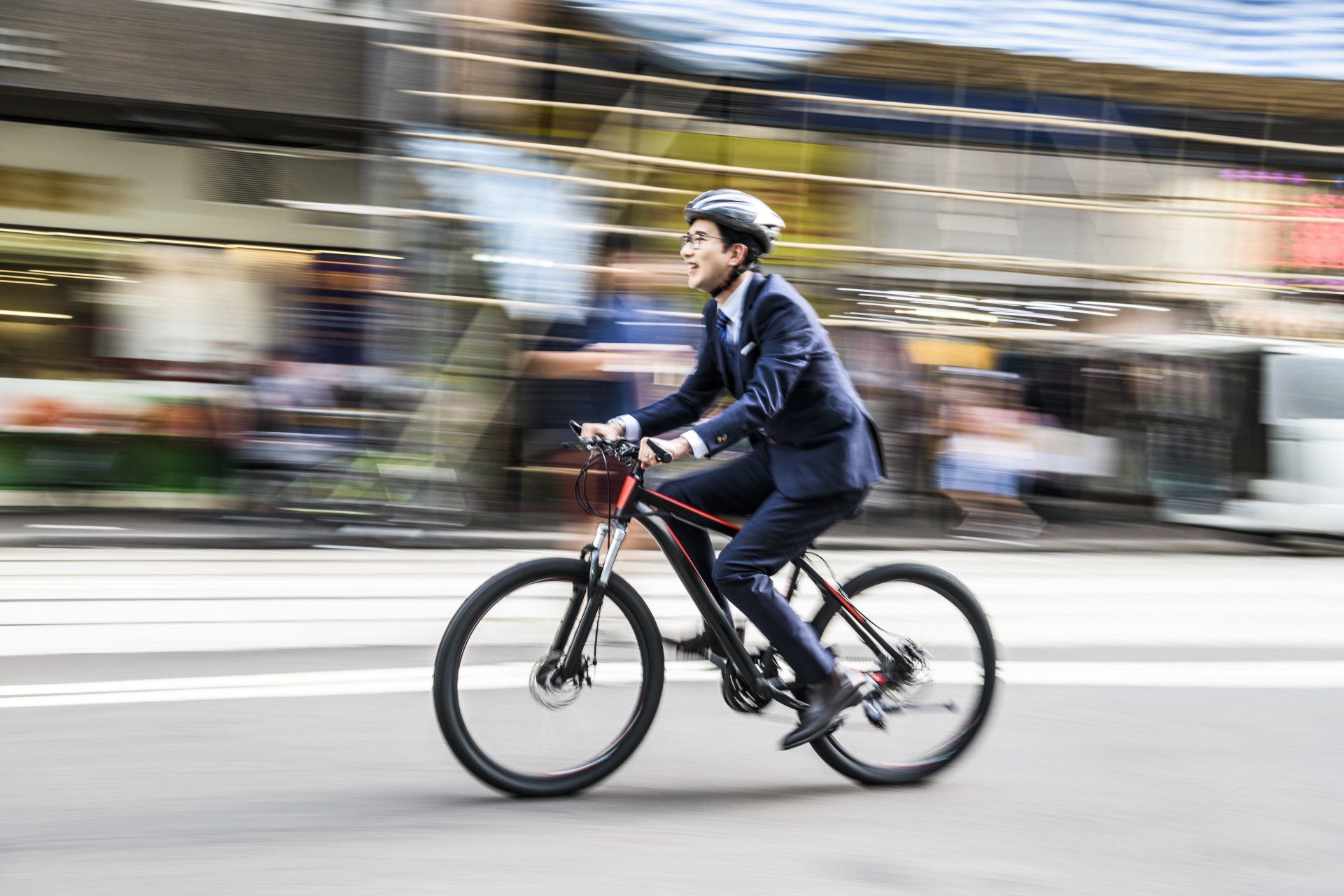 A man in a suit and helmet is riding a bicycle down a city street.