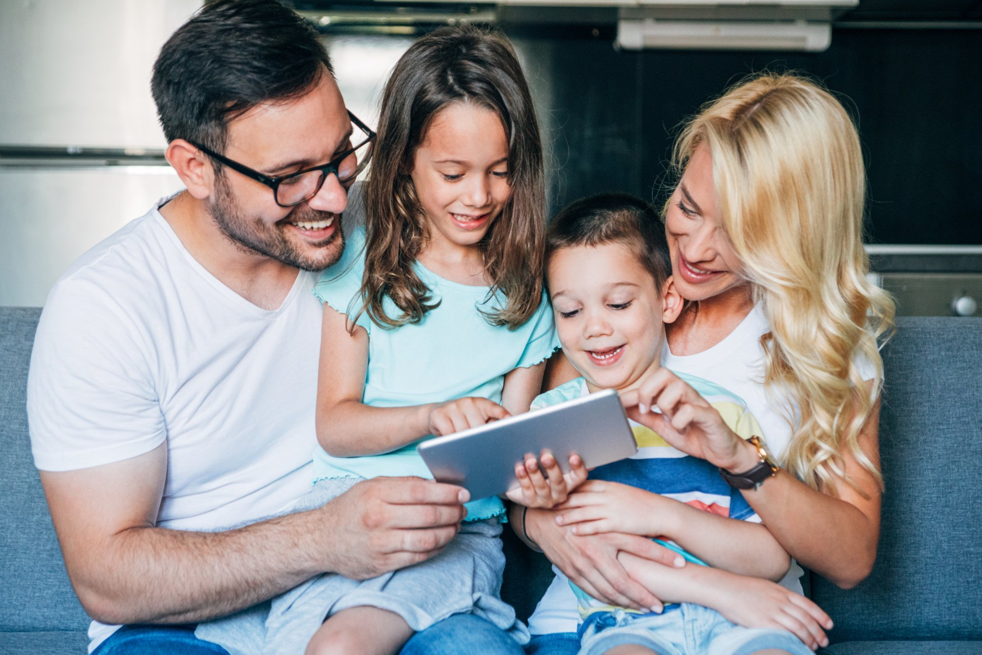 A family is sitting on a couch looking at a tablet.