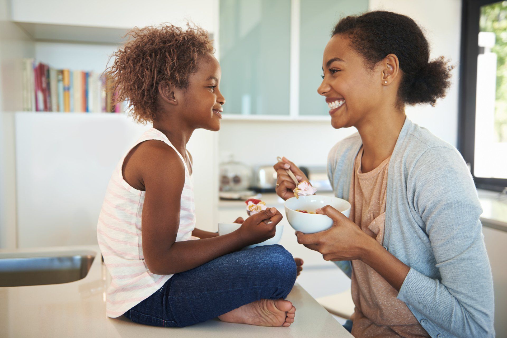 A woman and a child are sitting at a table eating cereal.