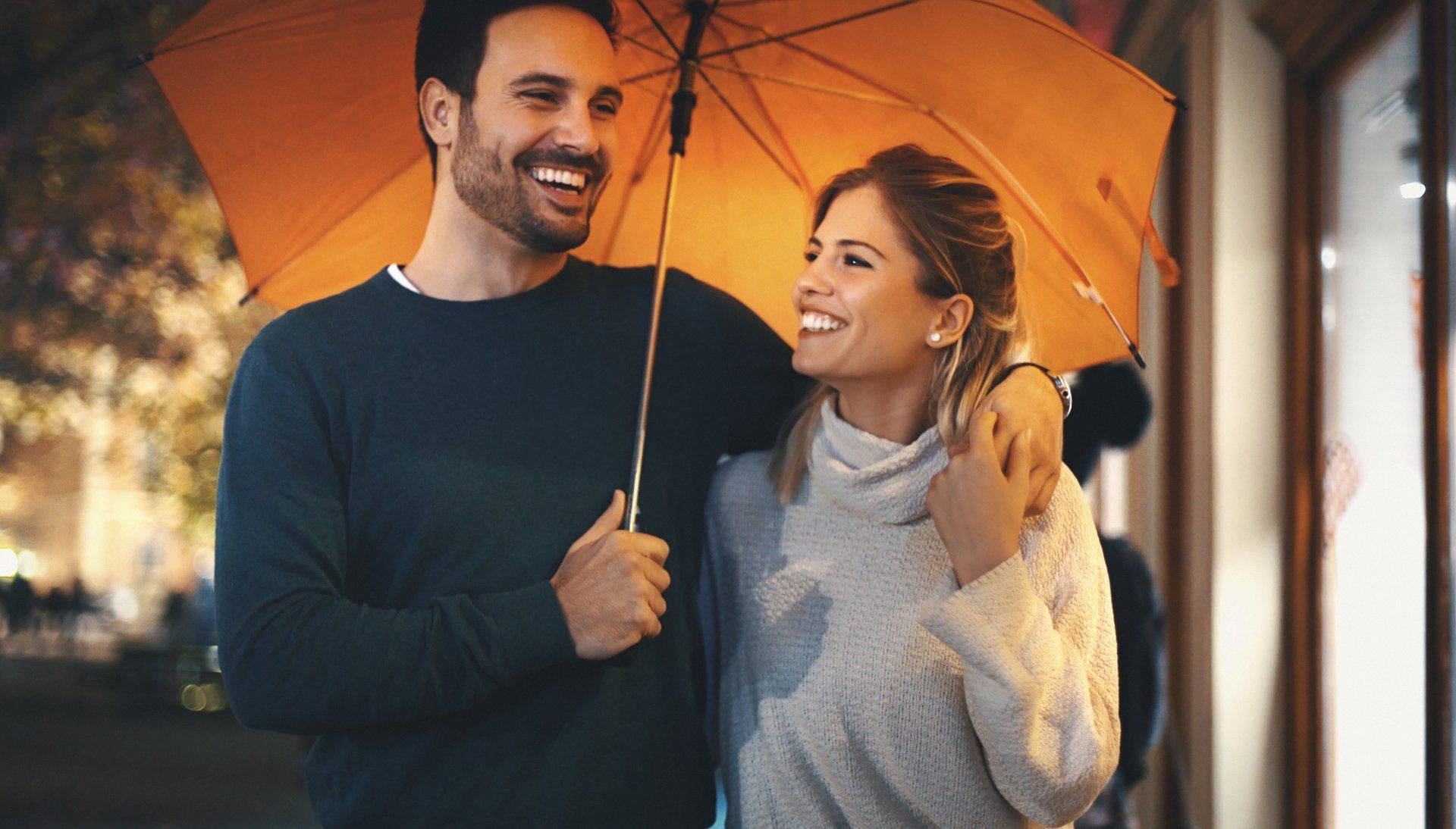 A man and a woman are holding an orange umbrella in the rain.
