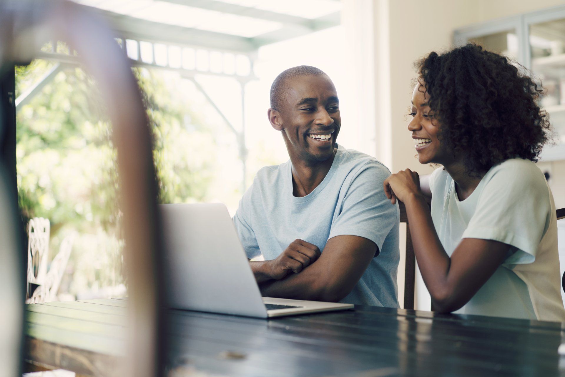 A man and a woman are sitting at a table looking at a laptop computer.