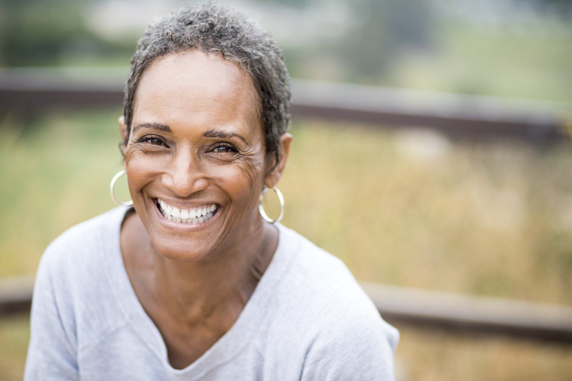 A woman with gray hair and hoop earrings is smiling for the camera.