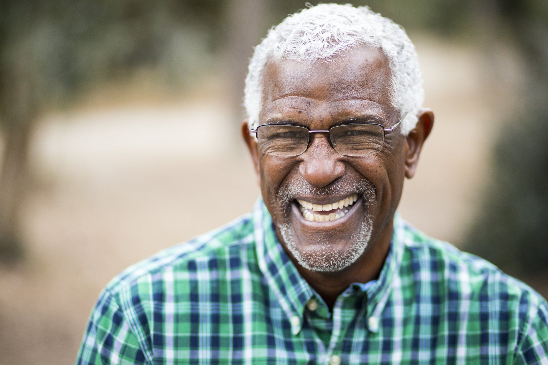 An older man wearing glasses and a plaid shirt is smiling.