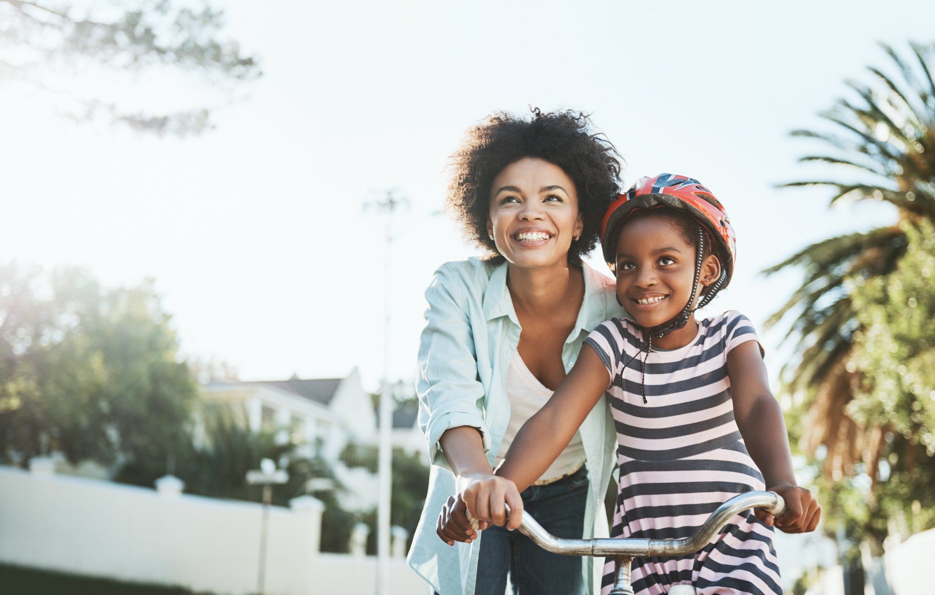 A woman is teaching a little girl how to ride a bike.