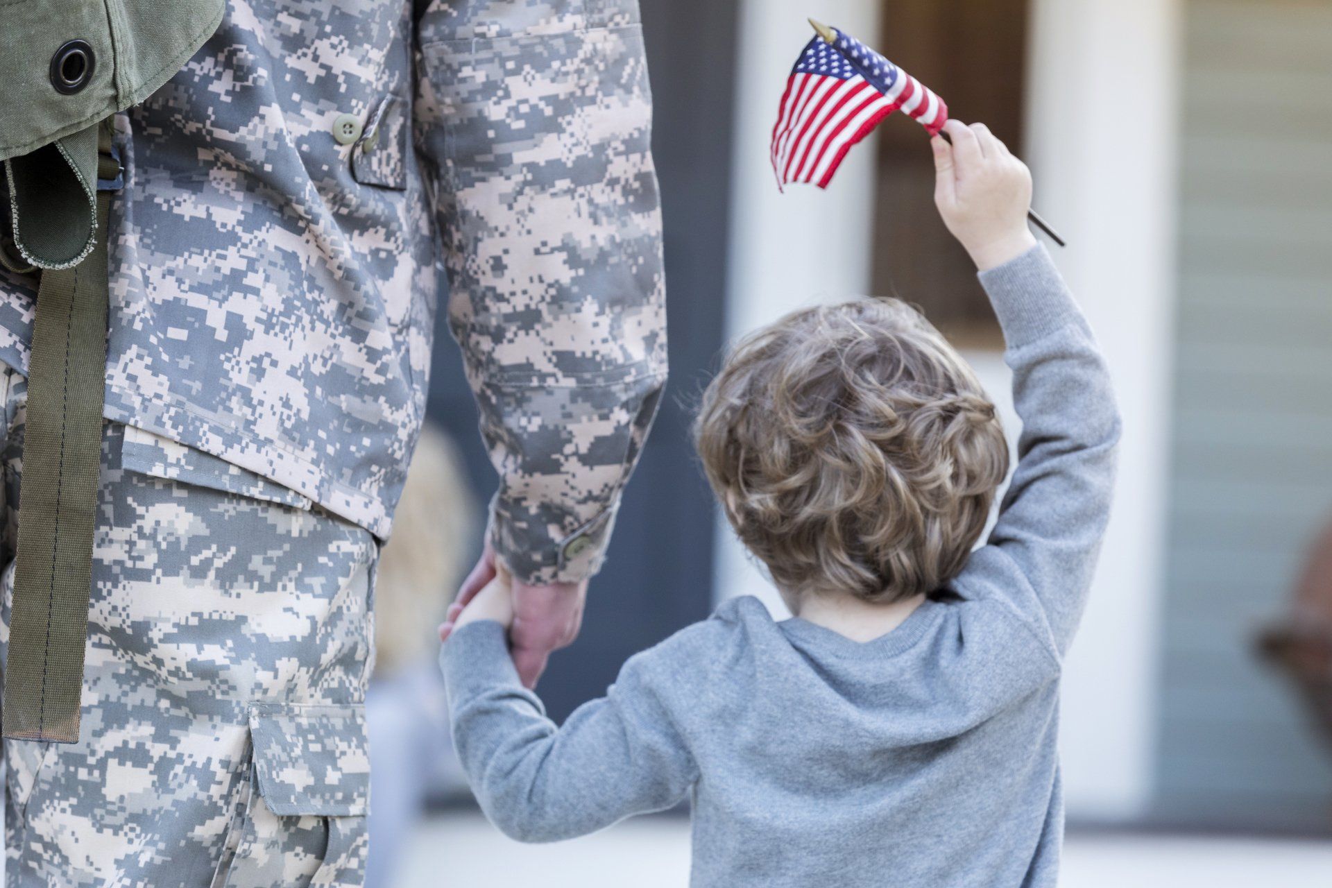 A soldier is holding the hand of a young boy who is waving an american flag.