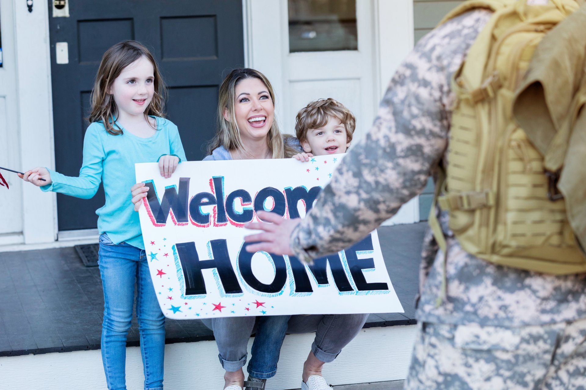 A soldier is holding a welcome home sign in front of a family.