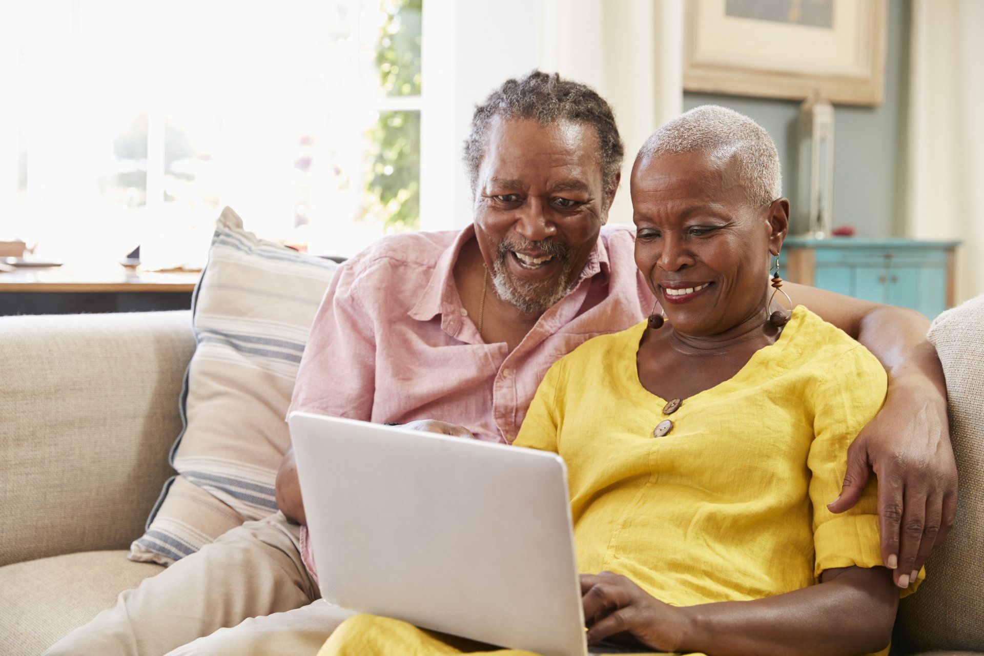 An elderly couple is sitting on a couch looking at a laptop computer.