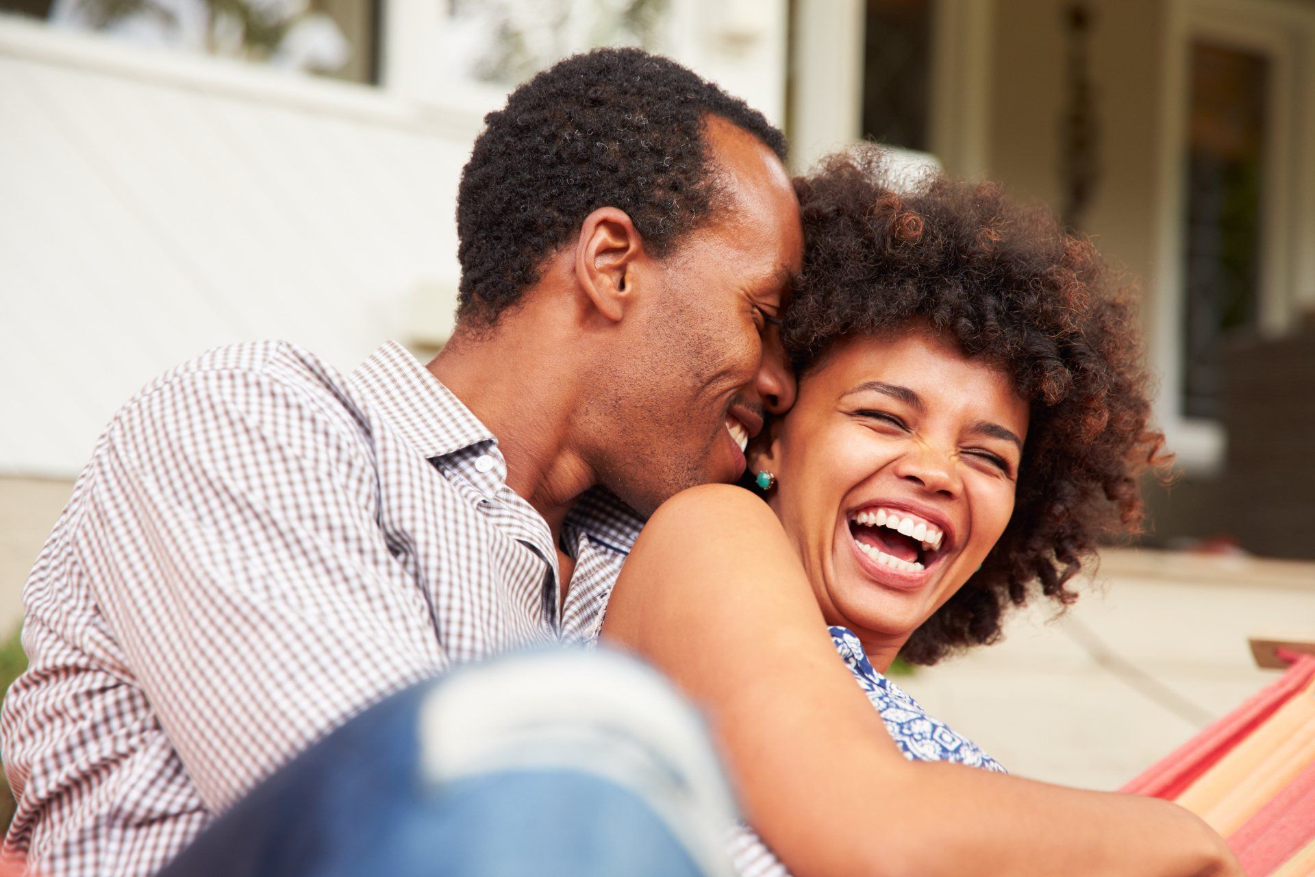 A man and a woman are sitting in a hammock and laughing.