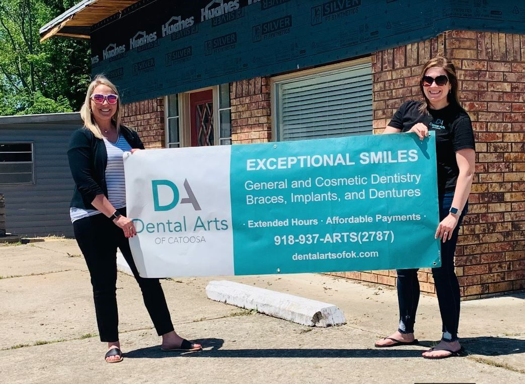 Two women are holding a sign in front of a brick building.