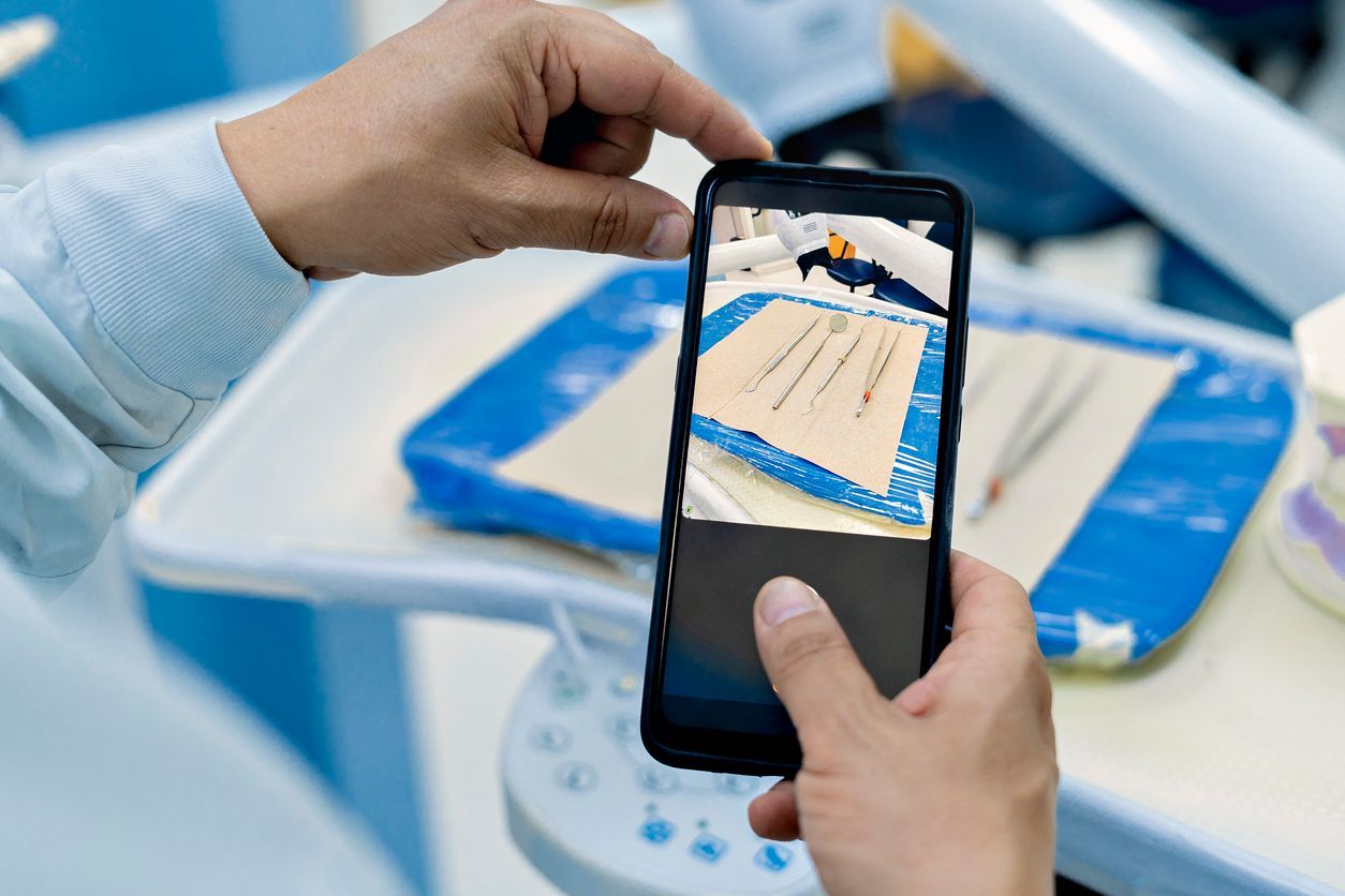 Person holding phone, taking photo of dental tools on tray in a dentist's office.