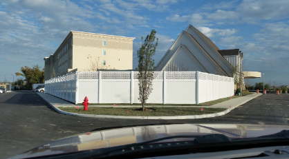 A woman is working on a fence with a wheelbarrow in the background.