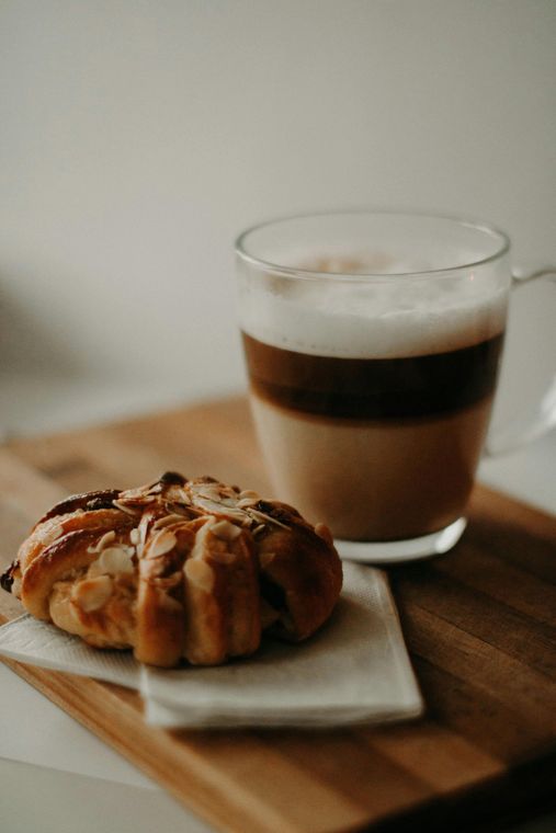 Latte with layered coffee and foam beside a pastry on a wooden board.