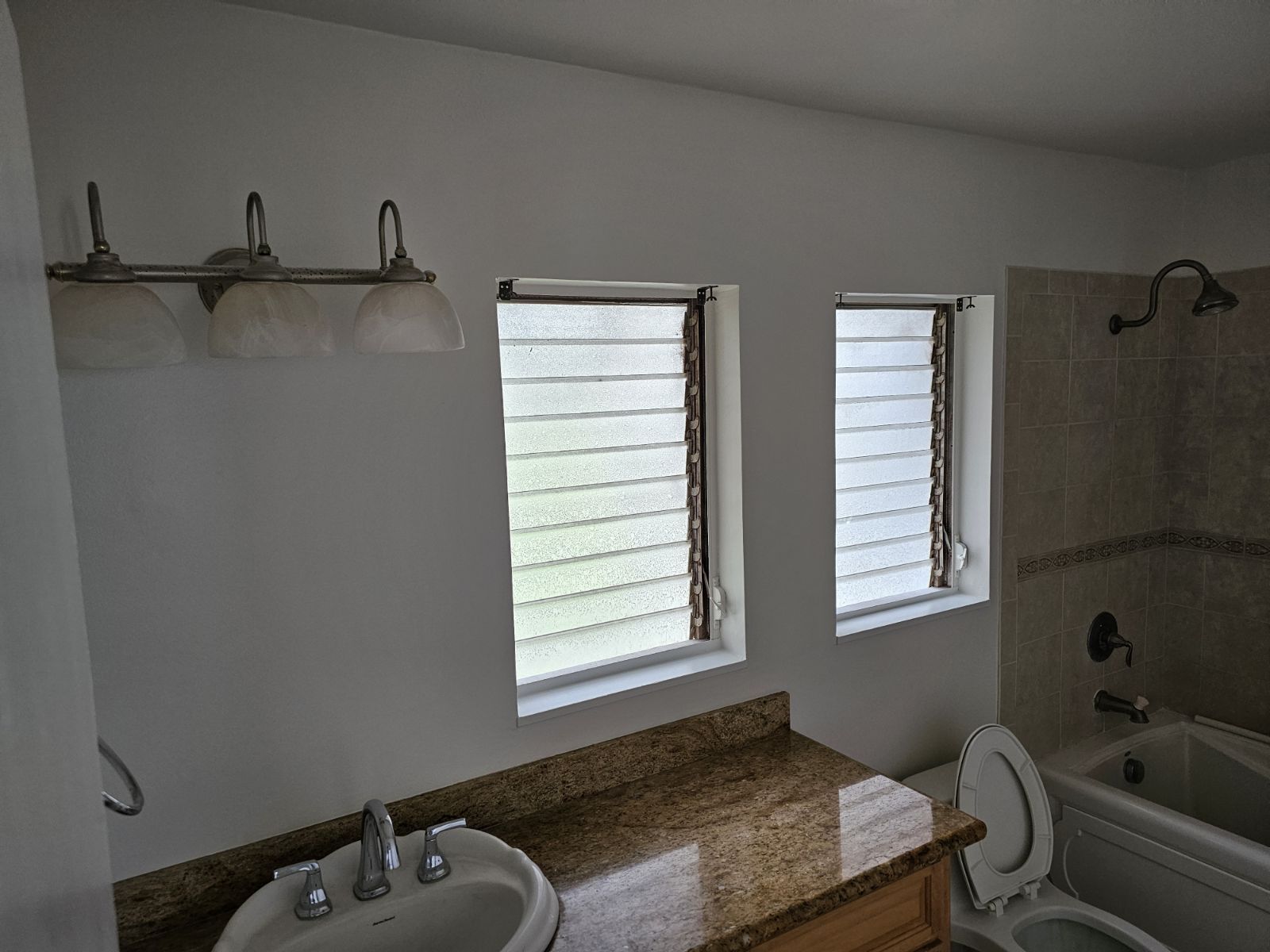 A bathroom with a sink a toilet and two windows