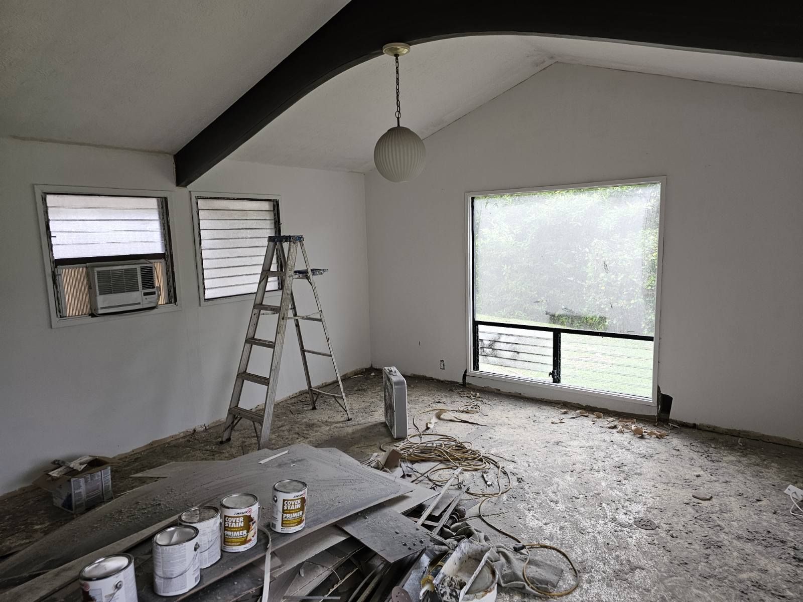 An empty room with a ladder and paint cans on the floor.