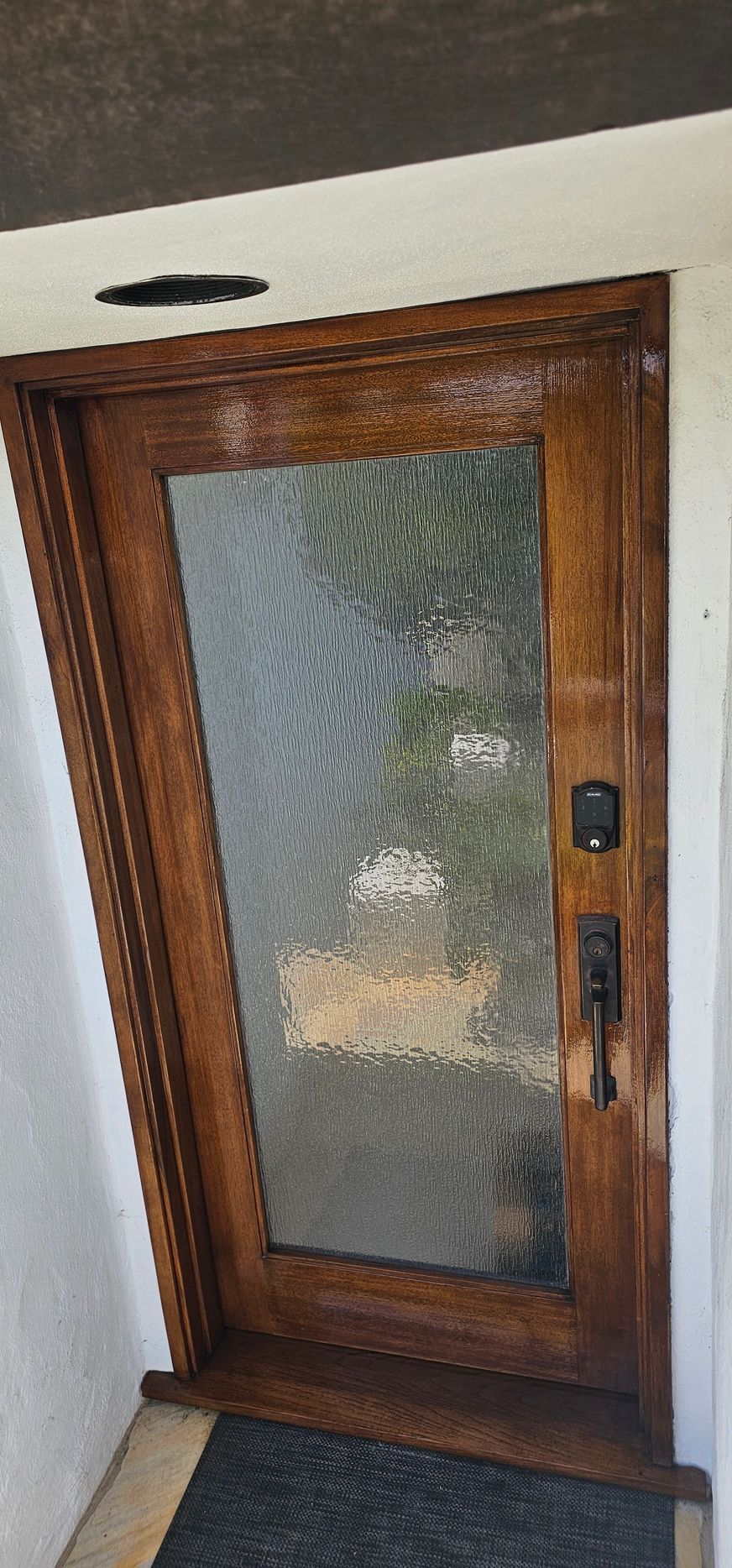 A wooden door with a glass window and a black mat on the floor.