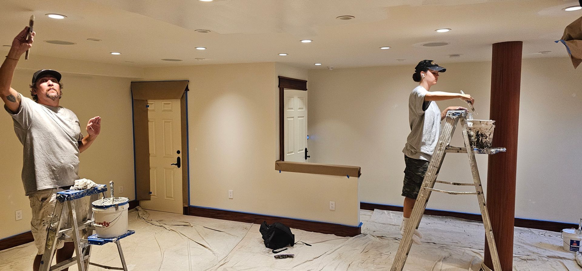 Two men are painting a room and one is on a ladder.