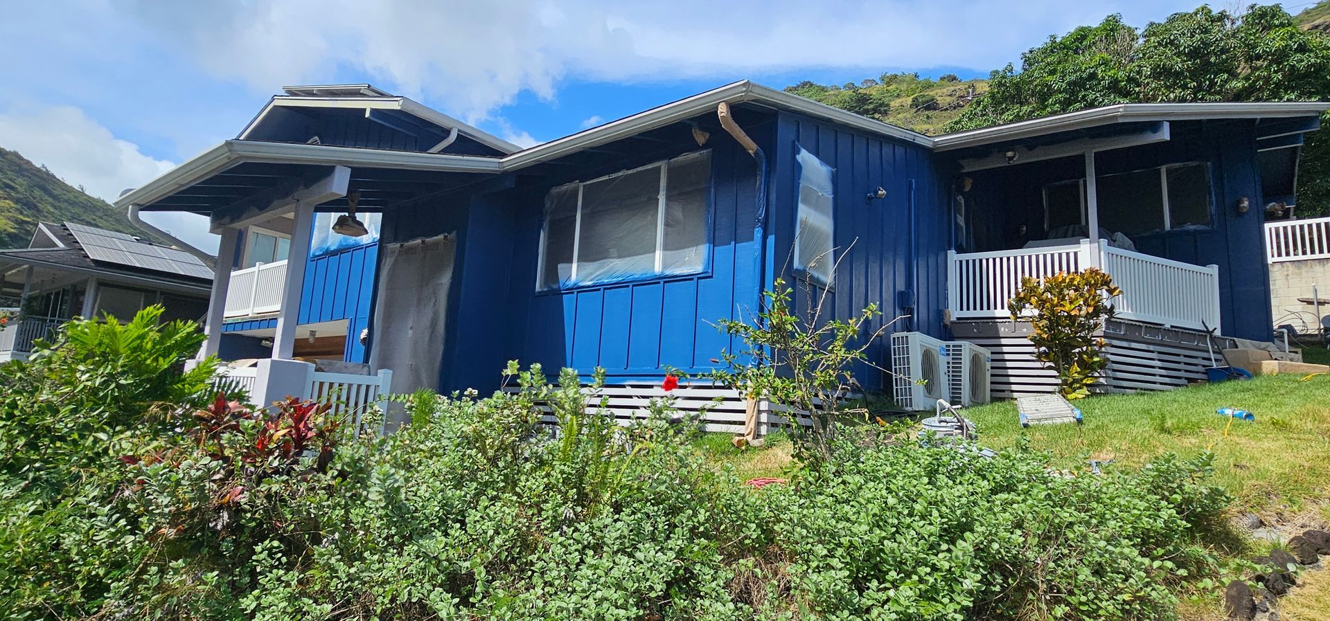 A blue house with a white porch is sitting on top of a grassy hill.