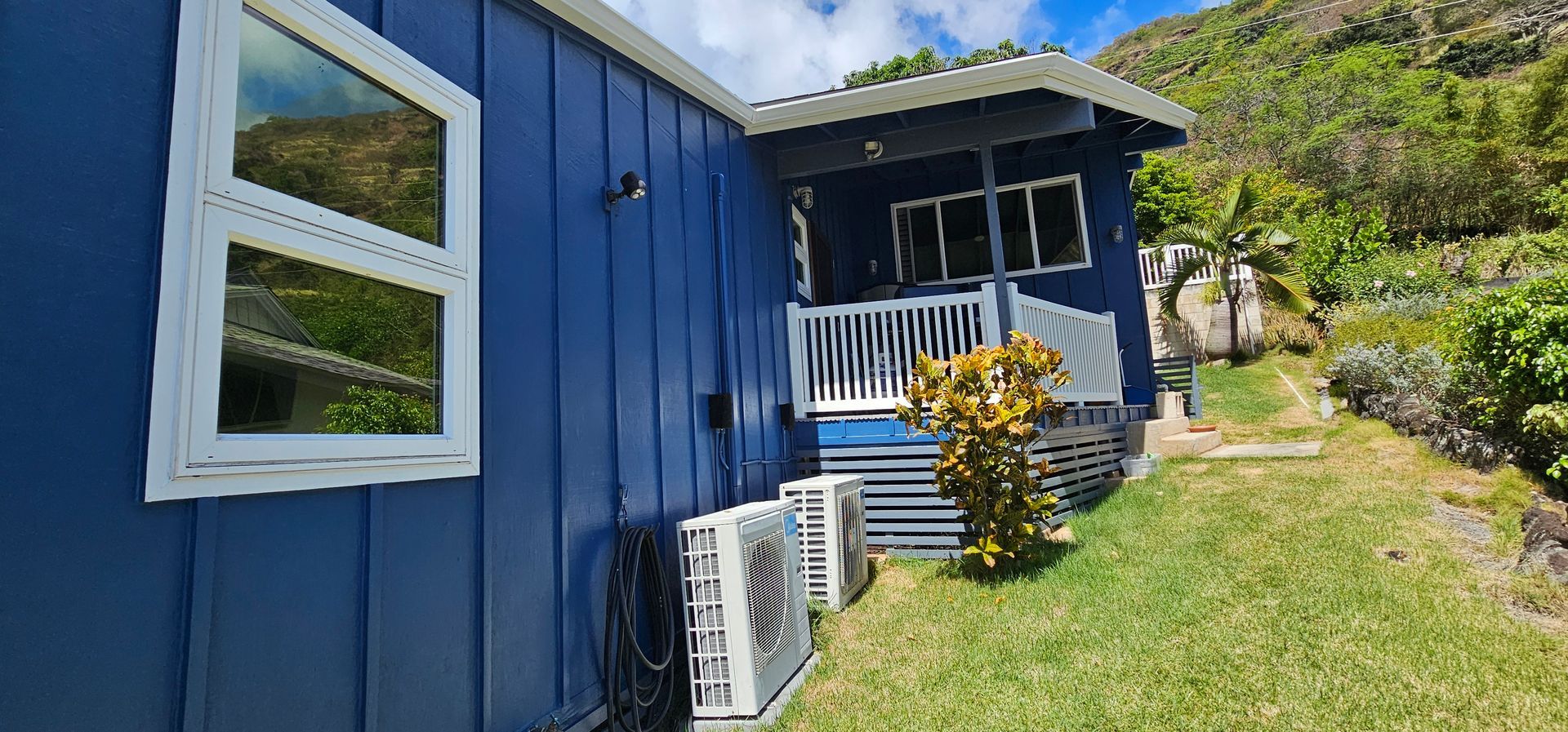 A blue house with a white porch is sitting on top of a grassy hill.