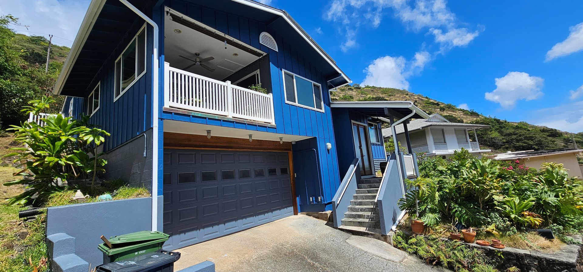 A blue house with a garage and stairs is sitting on top of a hill.