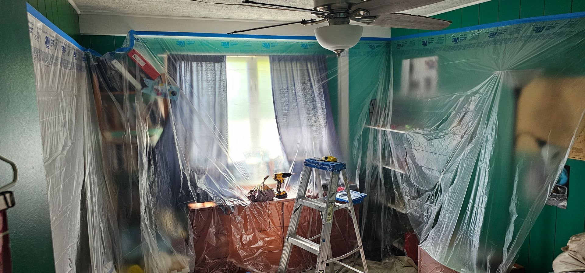 A room with green walls and a ceiling fan is being painted.