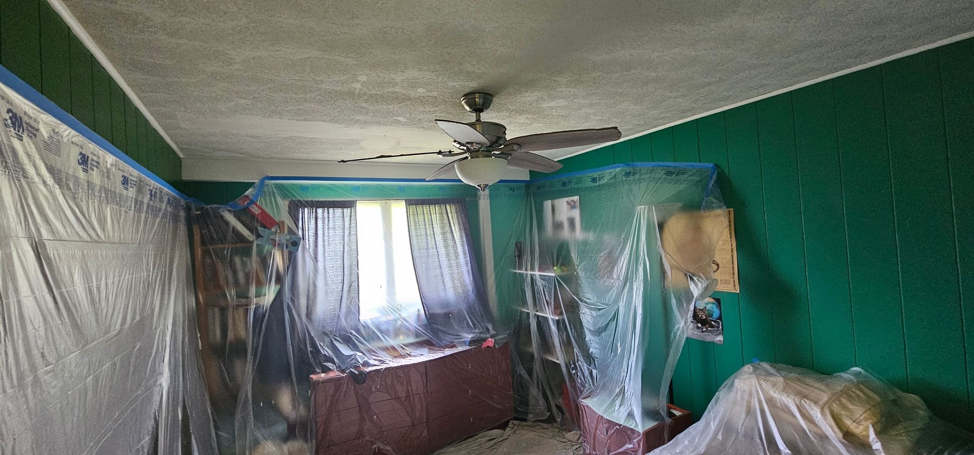 A room with green walls and a ceiling fan covered in plastic.