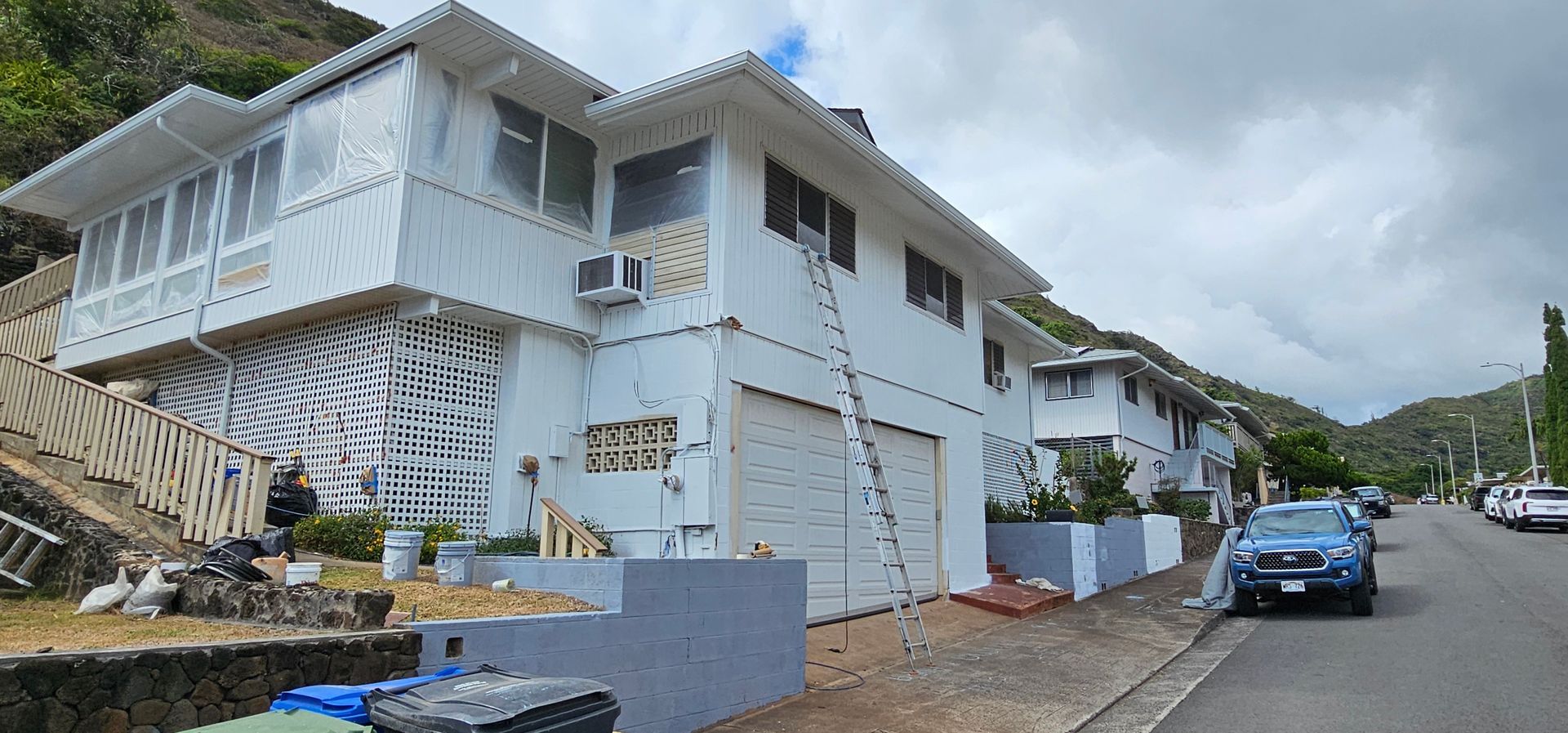 A white house with a ladder on the side of it is being painted.